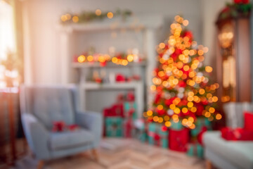 Naklejka na ściany i meble Blurred view of modern Christmas room interior with light bokeh background. Decorated glowing tree, armchair, fireplace with candles and gifts