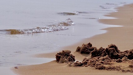 Closeup of a sandy beach and sunlit water waves shining and flowing the sand