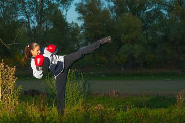 Young woman kickboxing and exercising in the nature on a sunny summer day