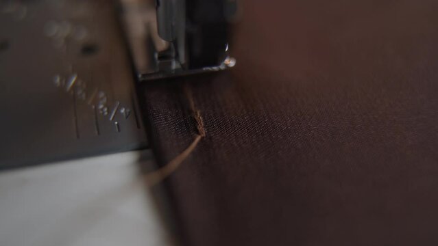 Sewing machine sews stitching thick thread on fabric with needle. Sewing machine operates on brown cloth macro. Clothing production process