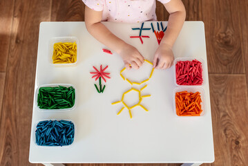 Child hands playing with dyed pasta for sensory play and craft activities. Learning colors activity for kids, activities Montessori, games for fine motor skills, play for toddler - obrazy, fototapety, plakaty