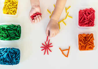 Child hands playing with dyed pasta for sensory play and craft activities. Learning colors activity for kids, activities Montessori, games for fine motor skills, play for toddler - obrazy, fototapety, plakaty