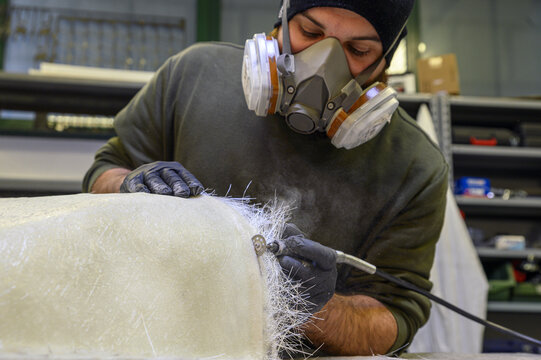 Installation of fiberglass: worker manually realizes a component in glass fiber with dremel for automotive use. Creation of an object in composite material using a mold. 
