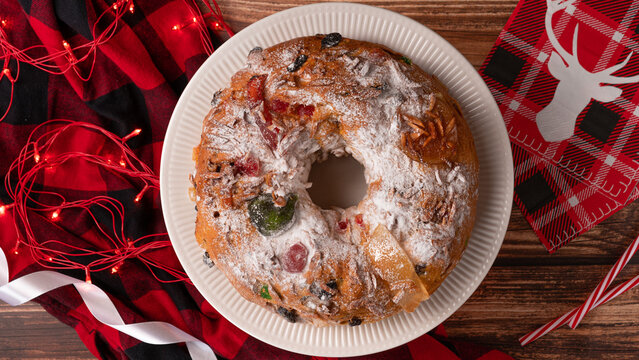 Portuguese Bolo Rei is a traditional Chrismas cake with fruits and icing on wooden table. Flat lay