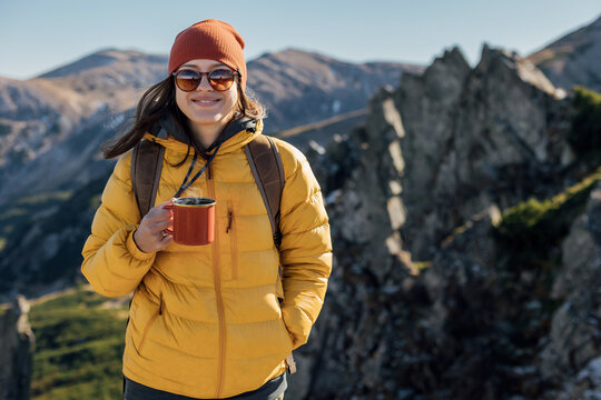 Portrait of a woman hiker standing with cup f tea on the slope of mountain ridge against mountains