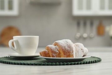 Croissant and cup of hot drink on white table in kitchen, space for text