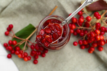 Spoon and jar with tasty viburnum jam on table, top view