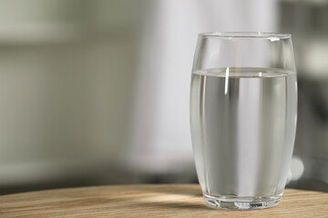 Glass of pure water on wooden table against blurred background, space for text