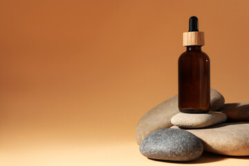 Bottle of face serum and spa stones on beige background, space for text