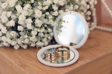 Pocket mirror, engagement rings and beautiful bouquet on wooden table. Wedding day