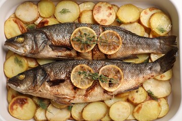 Baking tray with delicious baked sea bass fish and potatoes, top view