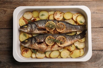 Baking tray with delicious baked sea bass fish and potatoes on wooden table, top view