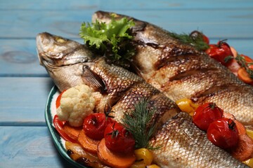 Plate with delicious roasted sea bass fish and vegetables on light blue wooden table, closeup