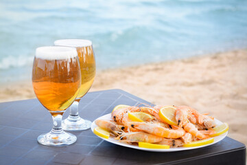 Cold beer in glasses and shrimps served with lemon on beach