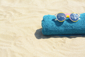 Towel with stylish sunglasses on sand outdoors, space for text. Beach accessories