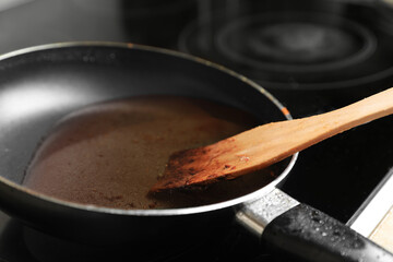 Frying pan with spatula and used cooking oil on stove, closeup