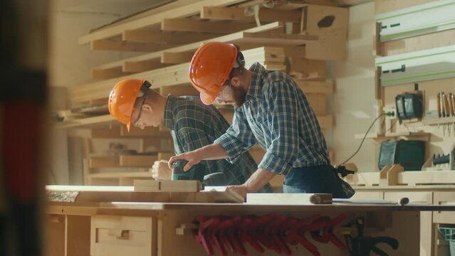 Carpenters Wearing Hard Hat on Head and Protective Glasses Working With a Piece of Furniture and a Lathe in Their Workshop.Woodworking. Manual Labor. Carpentry, Craftsmanship, and Handwork Concept.