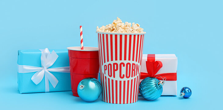 Bucket of popcorn, cup of soda drink, presents and Christmas balls on light blue background
