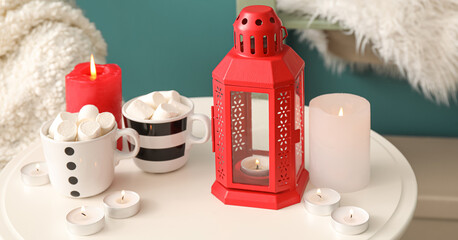 Christmas lantern with burning candles and cups of hot cocoa drink on table in living room