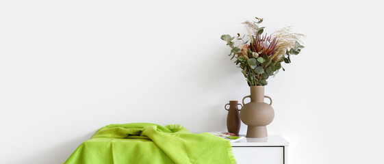 Vase with dried floral decor and green plaid on chest of drawers near white wall