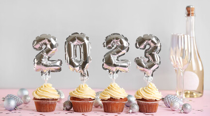 Christmas cupcakes with balloons and champagne on light background
