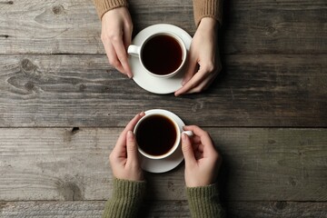 Women with cups of aromatic coffee at wooden table, top view