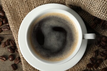 Cup of aromatic coffee and beans on wooden table, top view