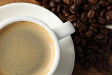 Cup of hot aromatic coffee and roasted beans on wooden table, top view. Space for text