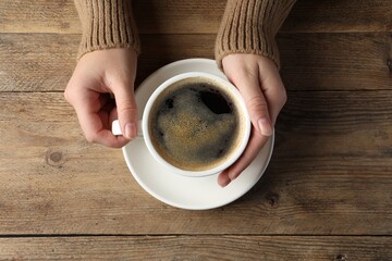 Woman with cup of hot aromatic coffee at wooden table, top view