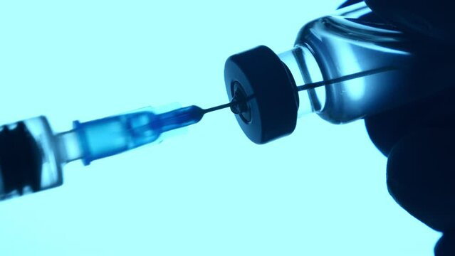Doctor injecting vaccine.Nurse doing vaccination. Syringe in hand wearing blue gloves fill in medicine from phial. Closeup