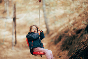 Little Girl Going Ziplining Enjoying it in Adventure Park. Courageous brave kid trying outdoors activities
 - obrazy, fototapety, plakaty