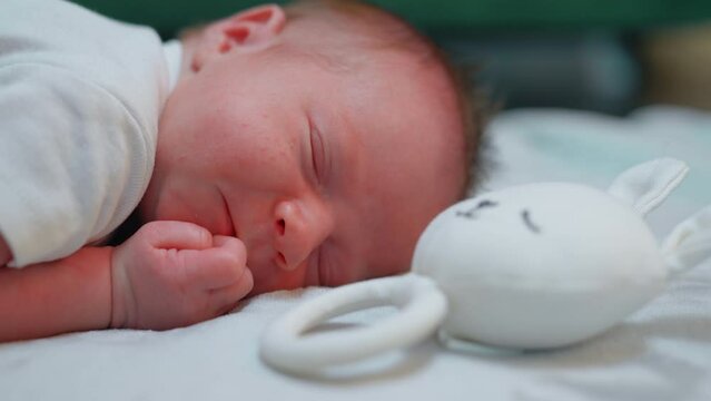 Closeup indoor shot of beautiful infant caucasian baby boy lying on his belly next to white, bunny-shaped rattle. Infancy and pregnancy concept. High quality 4k footage
