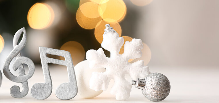 Violin clef, note sign, Christmas balls and snowflake on table against blurred lights - Powered by Adobe