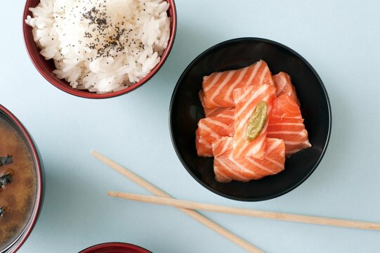 Top view closeup of salmon chunks, steamed rice and soy sauce in dark bowls on a table