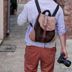 Unrecognizable Caucasian traveling tourist man in casual clothes travels with a system camera and a backpack through towns and cities in search of beautiful locations. There are no trademarks.