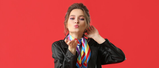 Beautiful stylish young woman blowing kiss on red background