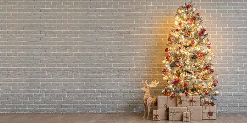 Beautiful Christmas tree with glowing lights, gifts and wooden reindeer near brick wall in room