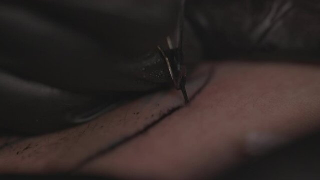 Zoomed slow motion close-up shot of a black tattoo line being stitching on white male's skin in a shallow depth of field 