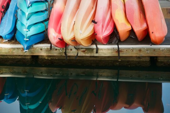 colorful rental kayaks lined up on edge of dock over water