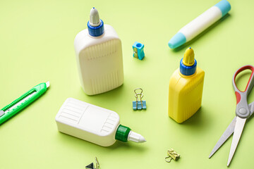 Bottles of glue and different stationery on green background