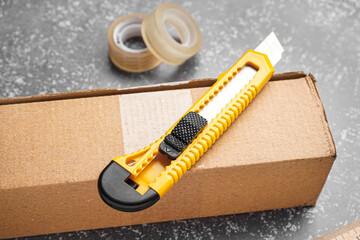 Utility knife with box, ruler and adhesive tapes on grunge background