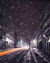 Fototapeta na wymiar The snow is falling gently and the light from the lamps along the street shine through it, making everything look hazy and romantic. The air is cold but there's a feeling of warmth emanating from all 
