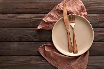 Table setting with cutlery in plate and napkin on wooden background