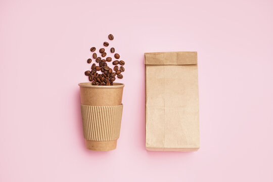 Paper cup with coffee beans and bag on pink background