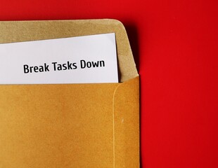 Document in office envelope with handwritten text note Break Tasks Down - means to break down tasks into smaller parts to make them easier to work on, focus on doing  just one work at a time