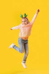 Happy little girl in reindeer horns jumping on yellow background