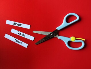 Scissors on red background, cut paper pieces with handwritten text - Break Tasks Down - means to...