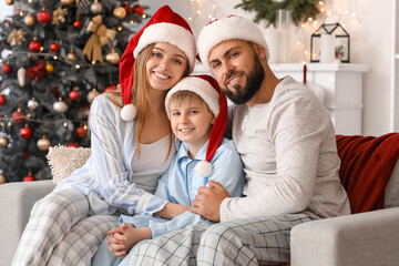 Happy parents with their little son in Santa hats sitting at home on Christmas eve