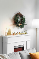 Beautiful Christmas wreath hanging on light wall near fireplace