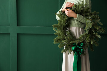 Woman with beautiful Christmas wreath near color wall